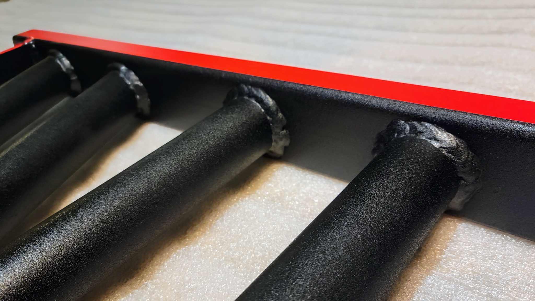 Close-up of BMF Swiss Barbell grip welds and red steel frame. Built for heavy-duty performance and customizable grip positions.